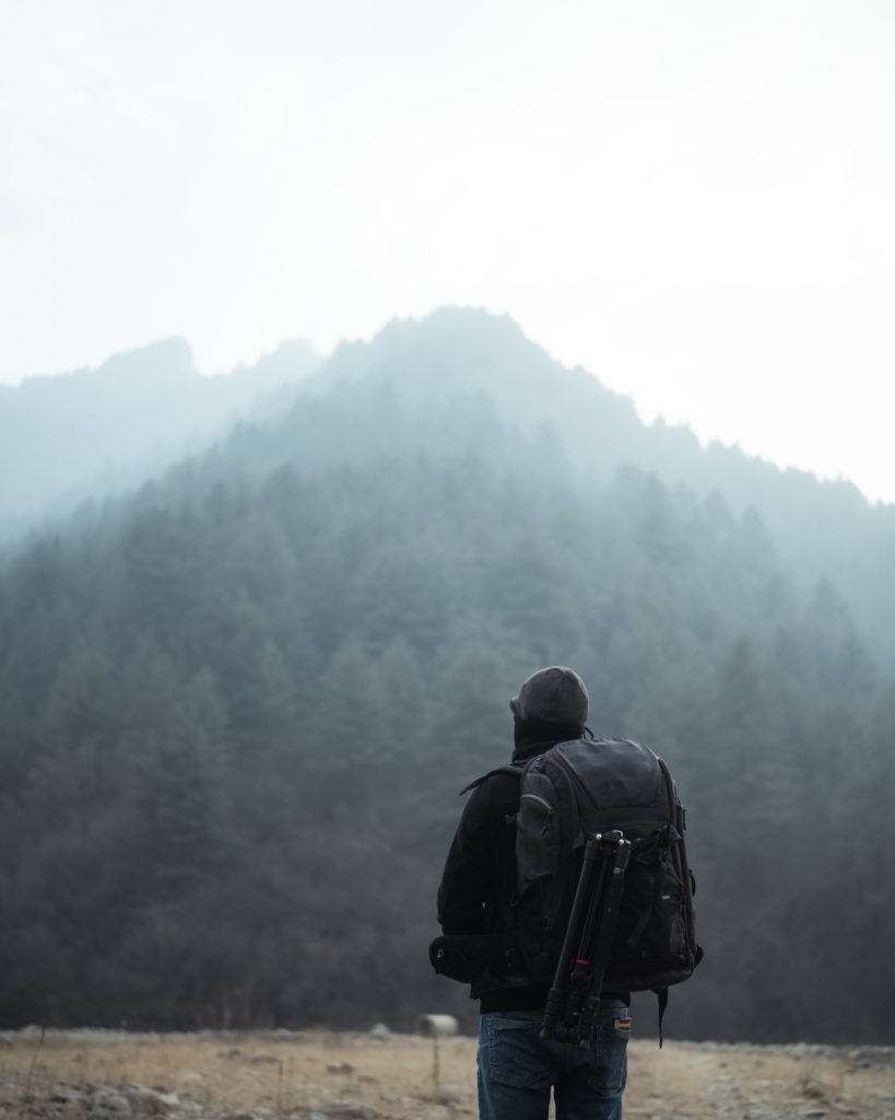 Photographer with a backpack standing before a misty mountain landscape