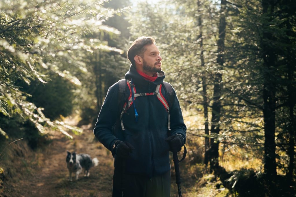 Man hiking with his dog in a sunlit forest